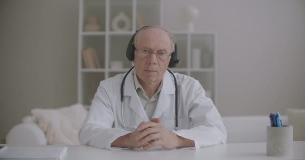 Terapeuta do sexo masculino idoso está ouvindo paciente durante consulta on-line, cabeça acenando, retrato do médico — Vídeo de Stock