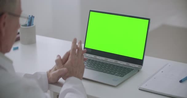 Il medico anziano sta consultando online, laptop con schermo verde sul tavolo, concetto chiave cromatico — Video Stock