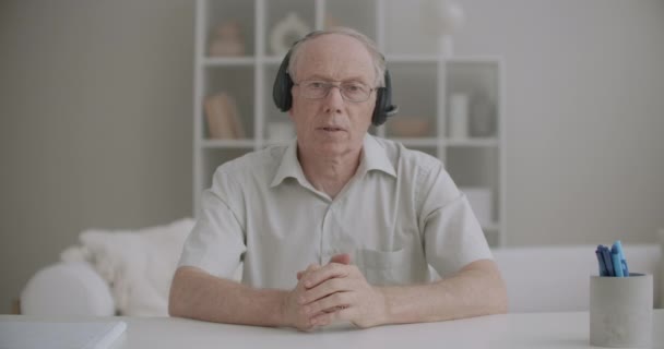 Professor do sexo masculino idoso com fones de ouvido está falando durante a educação on-line pela internet, retrato médio de falante idoso — Vídeo de Stock