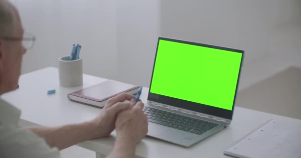 Retiree man is communicating online using laptop with video chat, green screen on pc for post-production — Stock Video