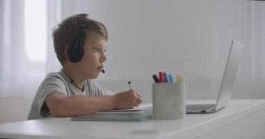 Evde okullu çocuklar için e-öğrenme, çocuk dizüstü bilgisayarda webinar izlemek ve telif defterinde yazmak, dil eğitimi