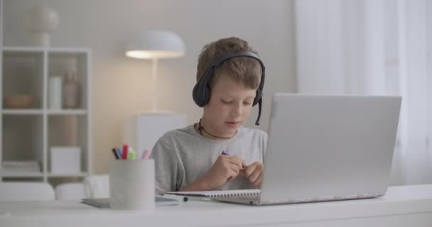 Μικρό αγόρι ζωγραφίζει από τσόχινα στυλό μένοντας στο σπίτι το Σαββατοκύριακο, ακούγοντας την εκμάθηση ήχου στα ακουστικά, φορητό υπολογιστή μπροστά του — Αρχείο Βίντεο