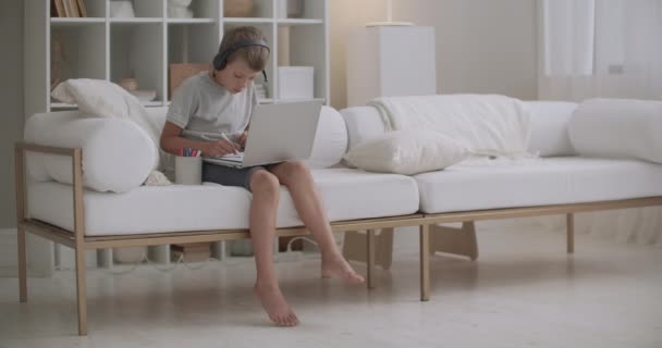 Schuljunge ruht zu Hause im Urlaub, zeichnet und schaut Videos per Laptop, sitzt allein — Stockvideo