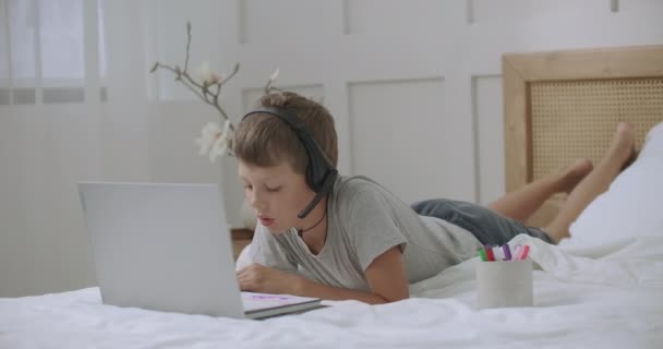 Anak sekolah sedang beristirahat di kamarnya, mendengarkan musik dengan headphone, terhubung ke laptop dan mewarnai gambar di atas kertas — Stok Video