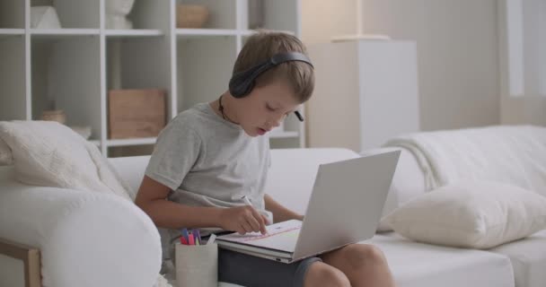 Garçon d'âge préscolaire apprend à dessiner à la maison, écouter de la musique et de la vidéo de formation à travers des écouteurs par ordinateur portable — Video