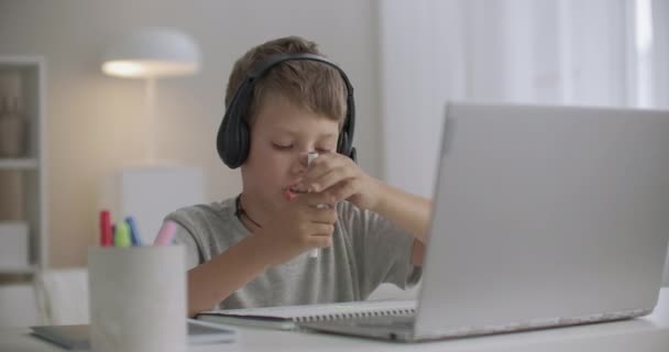 Školní chlapec kreslí doma a mluví přes internet s přítelem, pomocí notebooku a sluchátek s mikrofonem — Stock video