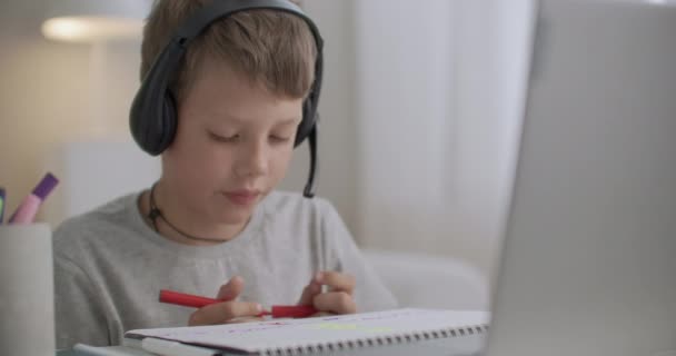 Portrét malého chlapce se sluchátky na hlavě, kreslící dítě sedí u stolu u svého pokoje — Stock video