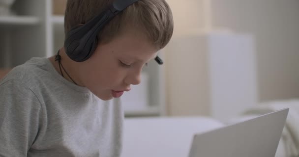 Porträtt av en liten pojke med hörlurar hemma, barnet ritar på copybook och lyssnar på musik — Stockvideo