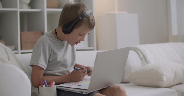 Barndom och modern teknik för kommunikation och utbildning, pojke sitter hemma ensam, rita och chatta via internet — Stockvideo