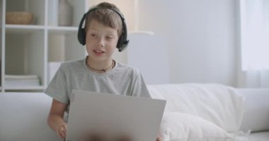 Çocuk, arkadaşlarıyla iletişim kurmak ve evde kalmak için internet kamerası ve kablosuz kulaklıkla modern dizüstü bilgisayar kullanıyor.