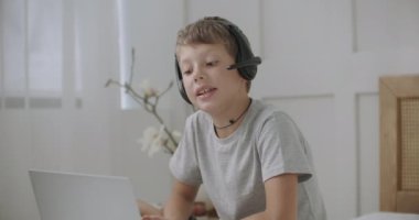 Küçük çocuk internet üzerinden biriyle konuşuyor. İnternet ve kulaklık takıyor. Tatilde evde kalıyor.