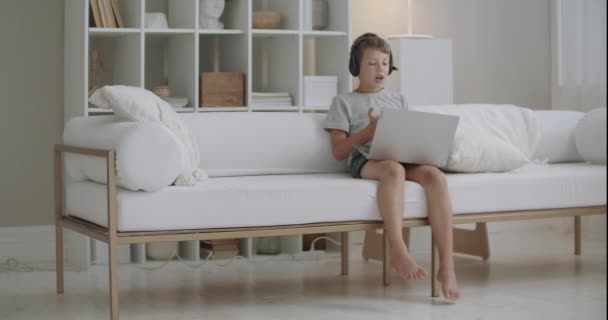Schulkind bleibt tagsüber im Urlaub allein zu Hause, chattet online im Internet, nutzt Notebook und Kopfhörer — Stockvideo