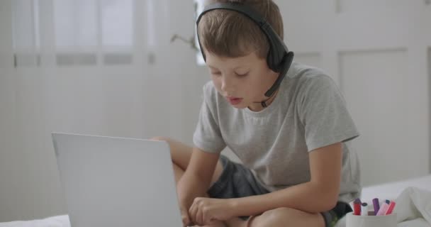 Menino estudante calmo está desenhando sozinho em seu quarto, vendo desenhos animados por laptop com fones de ouvido, entretendo de forma independente — Vídeo de Stock