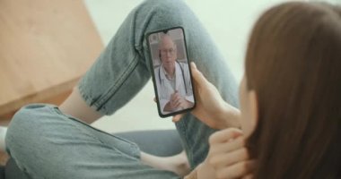 Kadın, internet üzerinden görüntülü konuşma kullanarak profesyonel doktorla olası belirtileri kontrol ediyor. Evde hasta olan genç bir kız doktoruyla video konferans uygulaması üzerinden konuşmak için akıllı telefon kullanıyor..