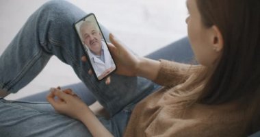 Kadın, internet üzerinden görüntülü konuşma kullanarak profesyonel doktorla olası belirtileri kontrol ediyor. Evde hasta olan genç bir kız doktoruyla video konferans uygulaması üzerinden konuşmak için akıllı telefon kullanıyor..