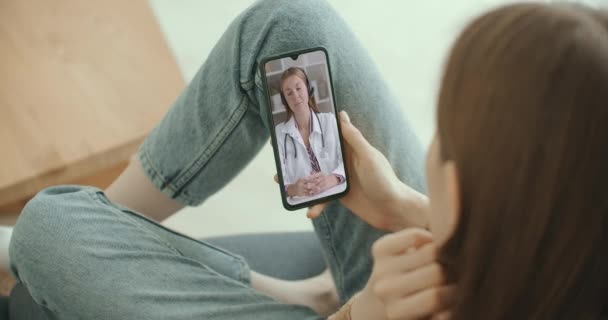 Женщина-ассистент носит белый халат, видео-гарнитуру, вызывающую дальнего пациента на смартфон. Врач разговаривает с клиентом через приложение виртуального чата. Телемедицина, дистанционные медицинские услуги — стоковое видео