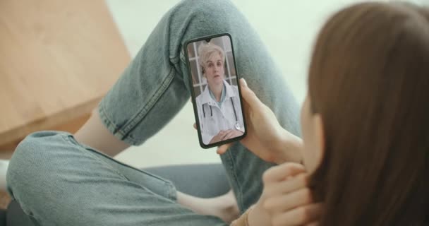 Kvinnlig medicinsk assistent bär vit rock, headset video ringer avlägsen patient på smartphone. Läkare pratar med klienten med hjälp av virtuell chatt telefon app. Telemedicin, distansvård — Stockvideo