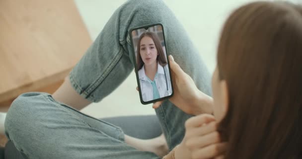 Asisten medis perempuan mengenakan mantel putih, video headset memanggil pasien jauh di smartphone. Dokter berbicara dengan klien menggunakan aplikasi telepon obrolan virtual. Telemedicine, layanan kesehatan terpencil — Stok Video