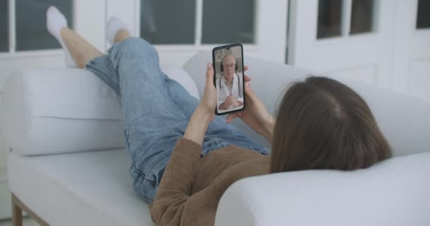 เด็กสาวป่วยที่บ้านโดยใช้สมาร์ทโฟนเพื่อพูดคุยกับแพทย์ของเธอผ่านทางแอพพลิเคชั่นการประชุมทางวิดีโอ ผู้หญิงมีบทสนทนากับแพทย์มืออาชีพ ใช้แอพพลิเคชั่นแชทวิดีโอออนไลน์ — วีดีโอสต็อก