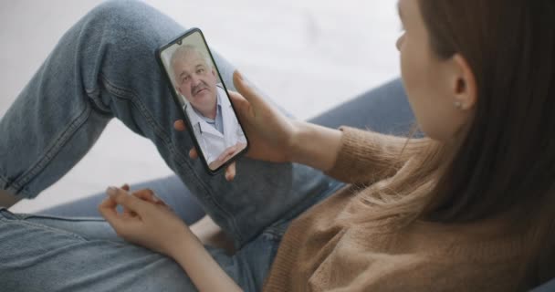 Woman checks possible symptoms with professional physician, using online video chat. Young girl sick at home using smartphone to talk to her doctor via video conference medical app. — Stock Video