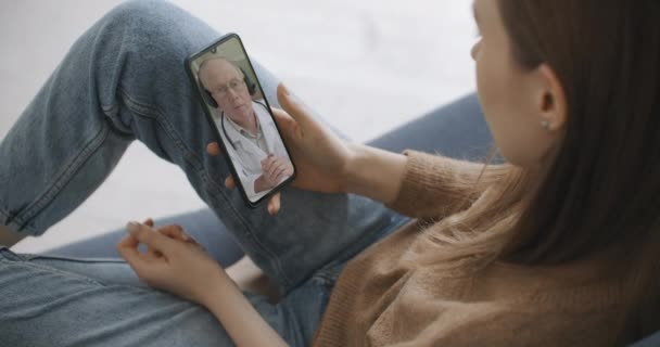 Жінка використовує медичний додаток на смартфоні, консультуючись з лікарем через відеоконференцію. Жінка використовує онлайн чат, щоб розмовляти з сімейним терапевтом і перевіряє можливі симптоми під час пандемії коронавірусу . — стокове відео