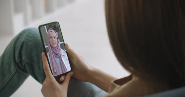 Vrouw met behulp van medische app op smartphone overleg met Arabische moslim vrouw in hijab arts via videoconferentie. Vrouw met behulp van online chat om te praten met familie therapeut en pandemie van coronavirus. — Stockvideo
