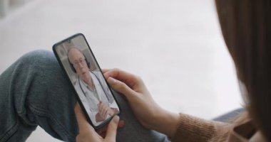 Kadın, internet üzerinden görüntülü konuşma kullanarak profesyonel doktorla olası belirtileri kontrol ediyor. Evde hasta olan genç bir kız doktoruyla video konferans uygulaması üzerinden konuşmak için akıllı telefon kullanıyor..