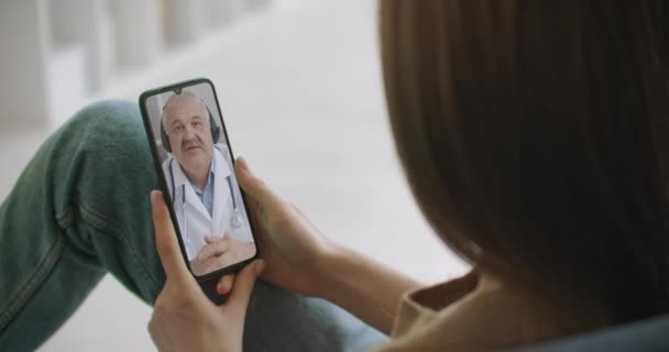 Mujer que utiliza la aplicación médica en la consulta de teléfonos inteligentes con el médico a través de videoconferencia. Mujer que utiliza el chat en línea para hablar con el terapeuta familiar y comprueba los posibles síntomas durante la pandemia de coronavirus. — Vídeos de Stock