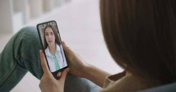 Vrouw controleert mogelijke symptomen met professionele arts, met behulp van online video chat. Jong meisje ziek thuis met behulp van smartphone om te praten met haar arts via videoconferentie medische app. — Stockvideo