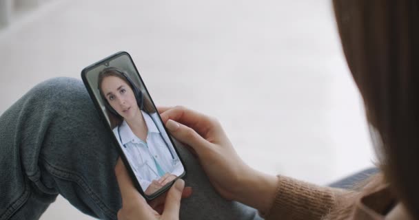Kvinna kontrollerar eventuella symtom med professionell läkare, med hjälp av online videochatt. Ung flicka sjuk hemma med hjälp av smartphone för att prata med sin läkare via video konferens medicinsk app. — Stockvideo