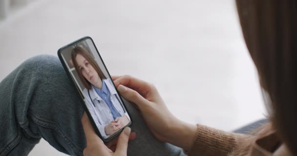 Vrouwelijke medische assistent draagt witte jas, headset video bellen verre patiënt op smartphone. Arts praten met de klant met behulp van virtuele chat telefoon app. Telegeneeskunde, gezondheidszorg op afstand — Stockvideo