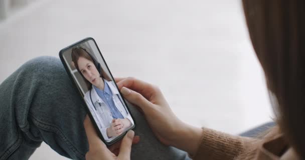 Female using online chat to talk with family therapist and checks possible symptoms during pandemic of coronavirus. Woman using medical app on smartphone consulting with doctor via video conference. — Stock Video