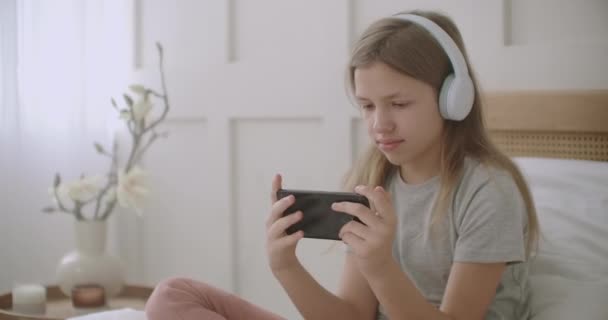 Tiener meisje is het luisteren van muziek door middel van een koptelefoon verbonden met smartphone door wifi, zitten in haar kamer thuis — Stockvideo