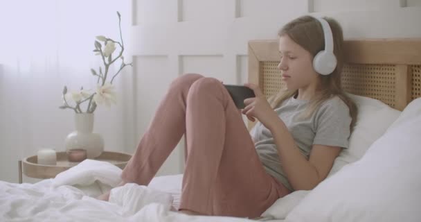 Kleine meisje muziekliefhebber luistert favoriete lied door smartphone en hoofdtelefoon in haar slaapkamer in vrije tijd in het weekend — Stockvideo