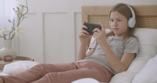 Nastolatka gra w grę w telefon komórkowy, leżąc na łóżku w domu po zajęciach szkolnych, dzieci z patologicznym korzystania z internetu — Wideo stockowe