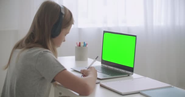 E-learning for schoolers by internet, girl is drawing in copybook listening teacher by videochat, green screen on laptop — Stock Video