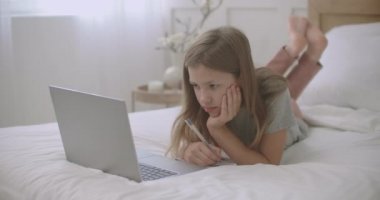 Sıkılmış çocuk ödevlerini defterde yapıyor, çevrimiçi dersler sırasında dizüstü bilgisayara bakıyor, evde öğreniyor.