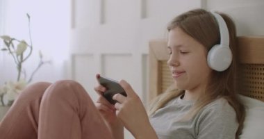Liseli kız akıllı telefonuyla sohbet ediyor, kulaklıkla dinliyor, yatak odasında kalıyor.