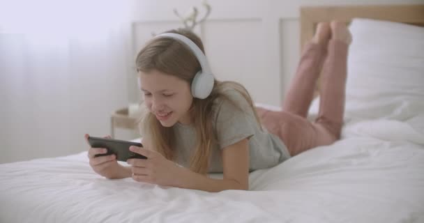 Menina da escola está usando o aplicativo no smartphone, deitado no quarto e falando, lazer das crianças no fim de semana — Vídeo de Stock
