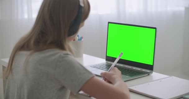 Teen girl sta imparando online seduto a tavola davanti al computer portatile con chiave cromatica in mostra, scrivendo in copybook a casa — Video Stock