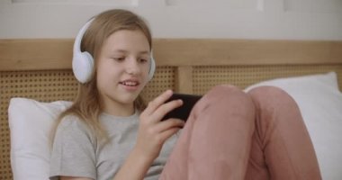 Genç kız evde cep telefonuyla internet oyunları oynuyor. Pazar sabahı yatak odasında uzanıyor ve internetten iletişim kuruyor.