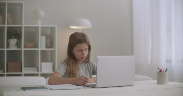 Scolaretta sta imparando online a casa, scrivere in copybook, fare dettatura, ascoltare insegnante dal computer portatile, educazione a distanza per gli scolari — Video Stock