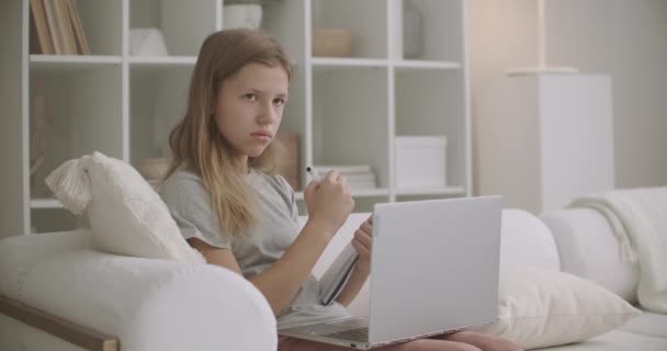 Chica de la escuela se está comunicando con el maestro por chat de vídeo en el ordenador portátil, haciendo la tarea en casa, la educación a distancia para la escuela secundaria — Vídeo de stock