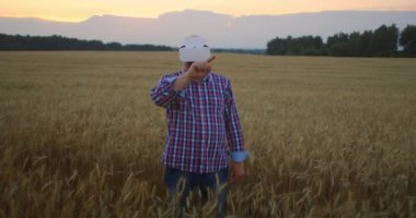 Sanal gerçeklik gözlüğü takan yaşlı bir adam buğday fırçasını jestlerle inceliyor. Mısır gevreği tarlasında dikil ve sanal gerçeklik kaskına jest yap.