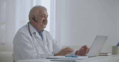 Hekim internette danışmanlık yapıyor, özel klinikte oturuyor, hastalarla konuşmak için dizüstü bilgisayar kullanıyor, teletıp teknolojisi