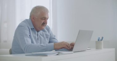 Orta yaşlı bir adam internet üzerinden e-posta teknolojisi kullanarak iletişim kuruyor, mesajlar yazıyor, evden çalışıyor.