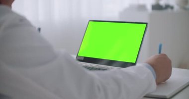 Teletıp hizmeti, en iyi tıp uzmanına danışmanlık, masada krom anahtar teknolojisi için yeşil ekranlı laptop, doktor notlar yazıyor.