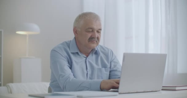 W wieku mężczyzna pracuje z laptopem w domu, odczuwając ostry ból zęba, dotykając policzka, problemy ze zdrowiem w dzień pracy — Wideo stockowe