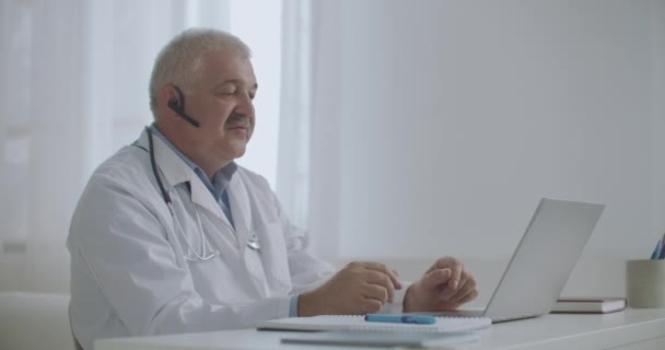 Terapeuta do sexo masculino está sentado em seu escritório de clínica médica e conversando on-line por videochat com pacientes ou colegas — Vídeo de Stock