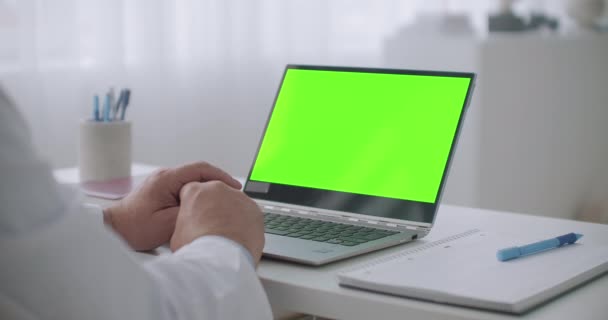 Ноутбук с зеленым экраном для хрома ключевых технологий на столе врача, консультирование в Интернете и просмотр вебинара, врач работает дистанционно — стоковое видео